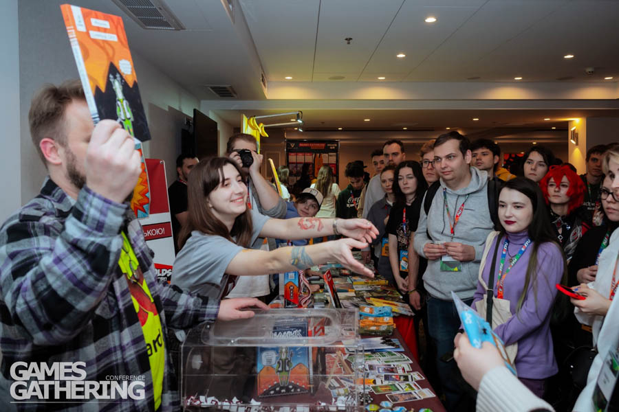 a room with men and women and a guy offering a magazine on his hands.